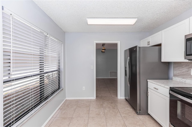 kitchen with light tile patterned floors, white cabinetry, appliances with stainless steel finishes, and a textured ceiling