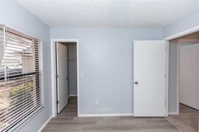 unfurnished bedroom with a spacious closet, a textured ceiling, and wood finished floors