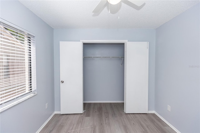 unfurnished bedroom with a textured ceiling, baseboards, a closet, and wood finished floors