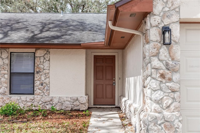 view of exterior entry with stone siding, a shingled roof, and an attached garage