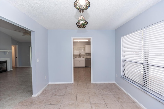 unfurnished dining area featuring baseboards, a textured ceiling, a fireplace, a sink, and light tile patterned flooring