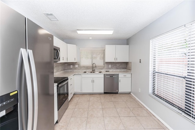 kitchen featuring light tile patterned floors, a sink, white cabinets, light countertops, and appliances with stainless steel finishes