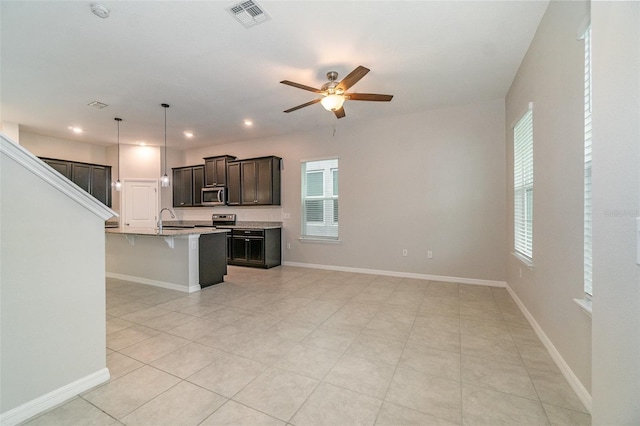 kitchen featuring decorative light fixtures, ceiling fan, a center island with sink, a breakfast bar, and appliances with stainless steel finishes