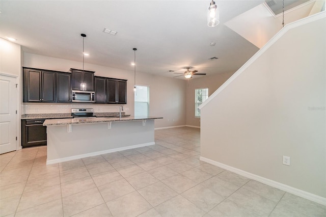 kitchen featuring ceiling fan, hanging light fixtures, stainless steel appliances, and a kitchen island with sink