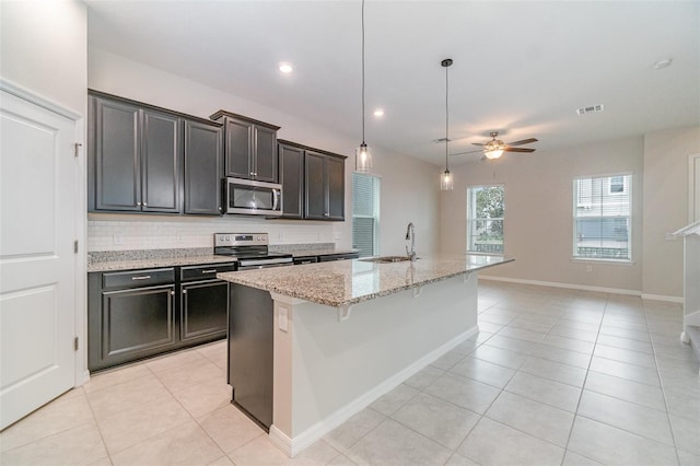 kitchen with ceiling fan, stainless steel appliances, a kitchen island with sink, light stone counters, and sink