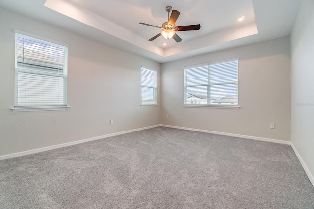 empty room with a raised ceiling, ceiling fan, and carpet