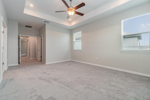 spare room with ceiling fan, a tray ceiling, and light carpet