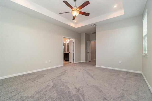 empty room featuring ceiling fan, light colored carpet, and a tray ceiling