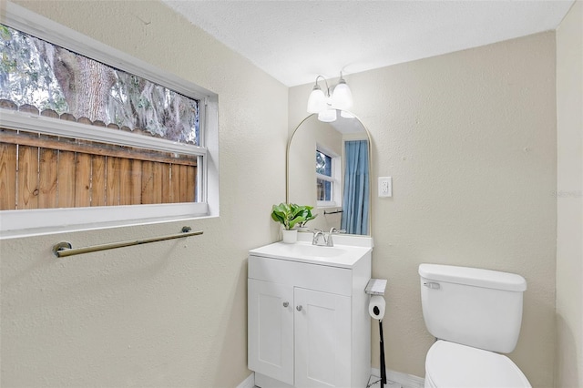 bathroom featuring a textured ceiling, a wealth of natural light, vanity, and toilet