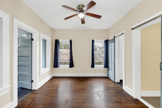 unfurnished bedroom featuring ceiling fan, a barn door, and dark hardwood / wood-style flooring