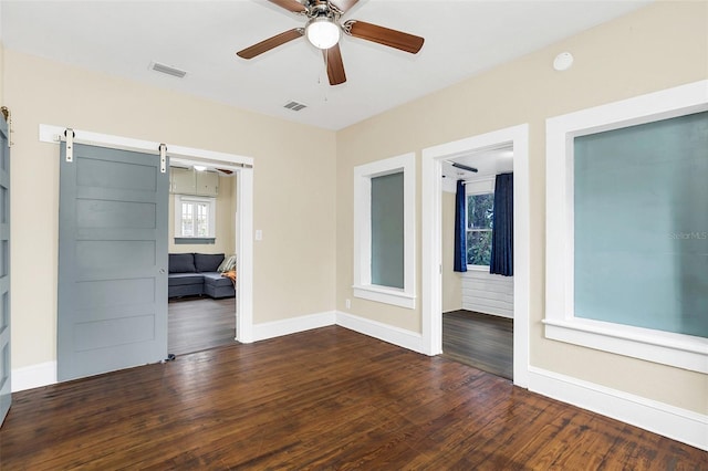 spare room with ceiling fan, a barn door, and dark hardwood / wood-style floors