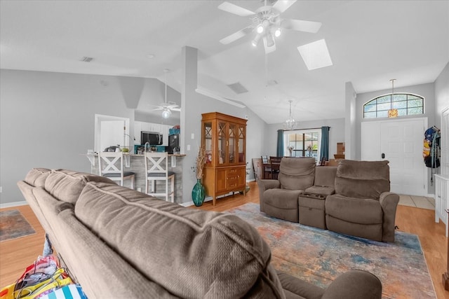 living room with ceiling fan with notable chandelier, vaulted ceiling with skylight, and light hardwood / wood-style flooring