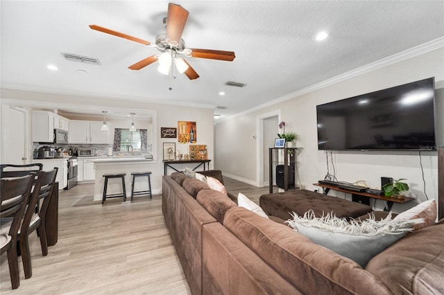 living room featuring ceiling fan, a textured ceiling, light hardwood / wood-style flooring, and ornamental molding