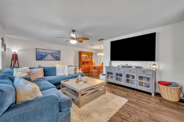 living room featuring ceiling fan with notable chandelier, a textured ceiling, and hardwood / wood-style floors