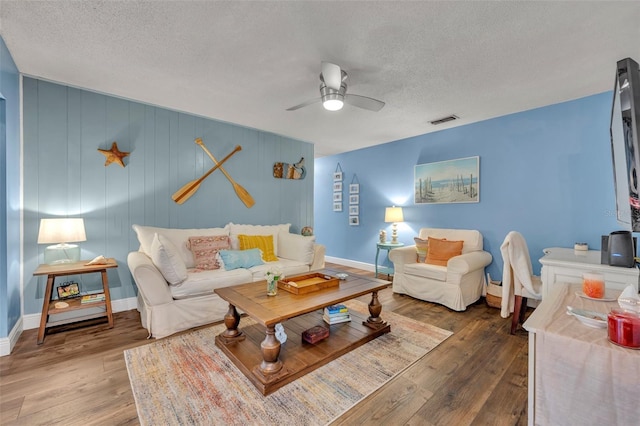 living room with a textured ceiling, ceiling fan, and wood-type flooring