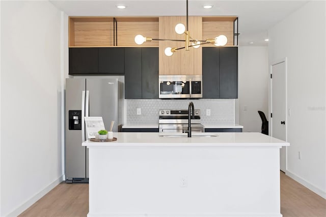 kitchen with hanging light fixtures, a kitchen island with sink, appliances with stainless steel finishes, and light wood-type flooring