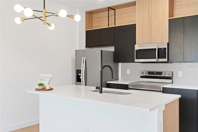 kitchen featuring an island with sink, stainless steel appliances, hanging light fixtures, light hardwood / wood-style flooring, and sink