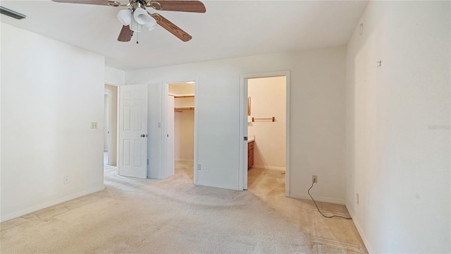 unfurnished bedroom with ensuite bath, a walk in closet, a closet, ceiling fan, and light colored carpet