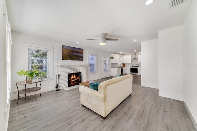 living room featuring a fireplace, light wood-type flooring, and ceiling fan