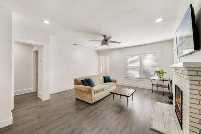 living room with a brick fireplace, ceiling fan, and wood-type flooring