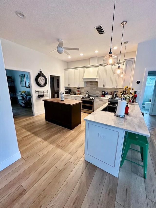 kitchen featuring double oven range, a center island, decorative light fixtures, custom range hood, and sink