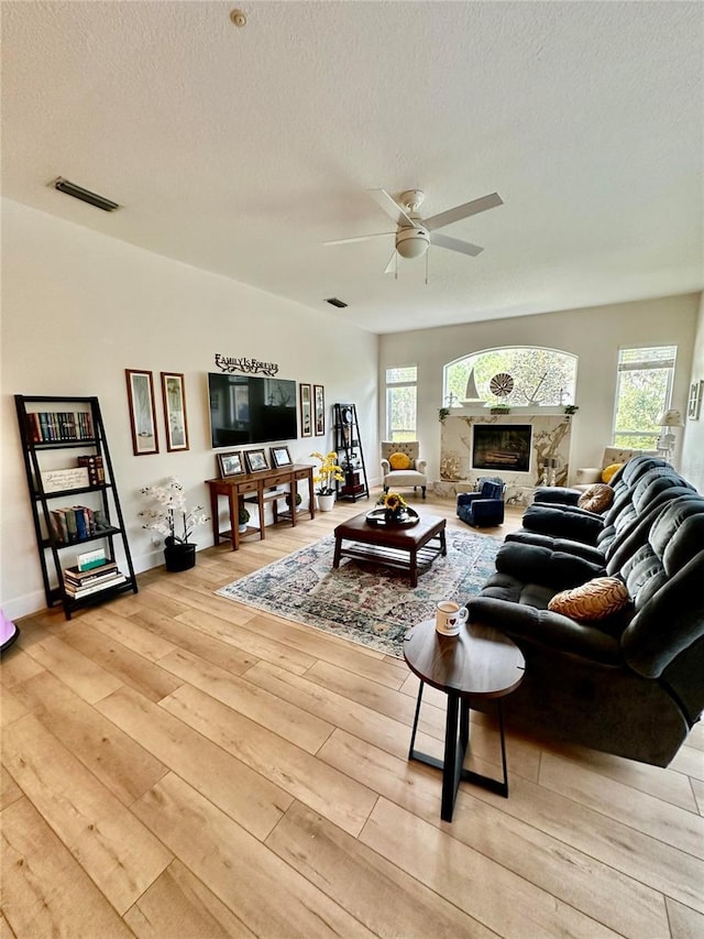 living room with a textured ceiling, ceiling fan, and light hardwood / wood-style floors