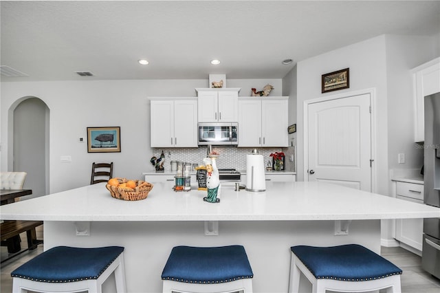 kitchen featuring white cabinetry, a kitchen bar, tasteful backsplash, and a large island