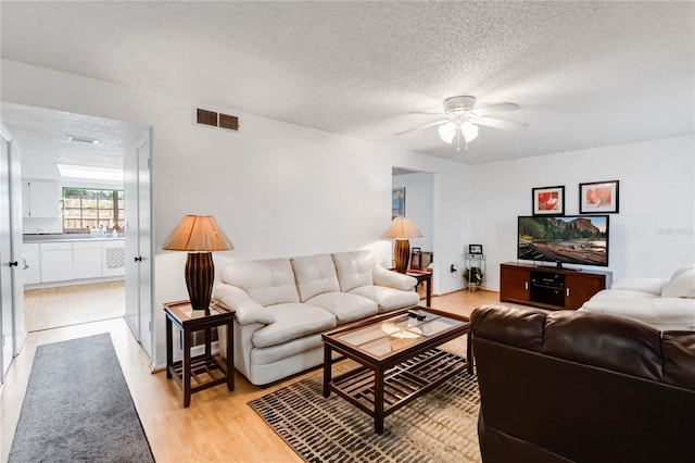 living room featuring light wood-type flooring, ceiling fan, and a textured ceiling