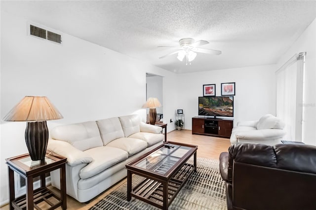 living room featuring ceiling fan, light wood-type flooring, and a textured ceiling