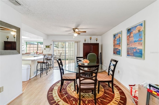 dining area featuring ceiling fan, light wood-type flooring, and a textured ceiling