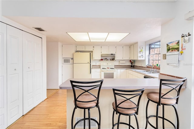 kitchen with light wood-type flooring, sink, white appliances, and a kitchen bar