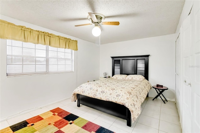 bedroom with ceiling fan, light tile patterned floors, a closet, and a textured ceiling