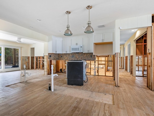 kitchen featuring backsplash, light hardwood / wood-style floors, white cabinetry, hanging light fixtures, and a breakfast bar area