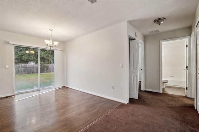 empty room with a textured ceiling, an inviting chandelier, and dark carpet