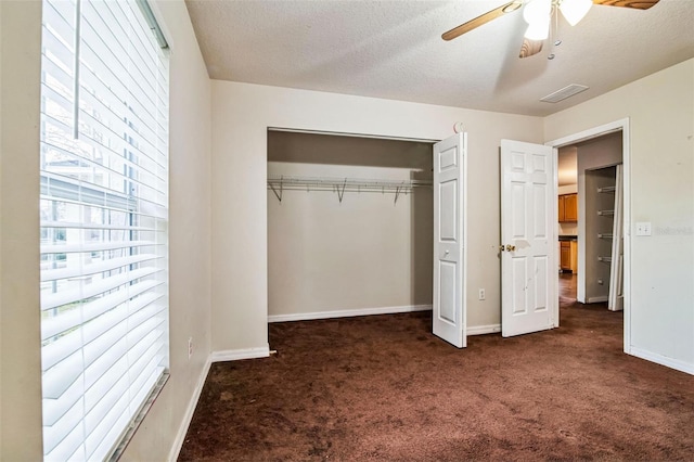 unfurnished bedroom featuring ceiling fan, a closet, a textured ceiling, and dark carpet