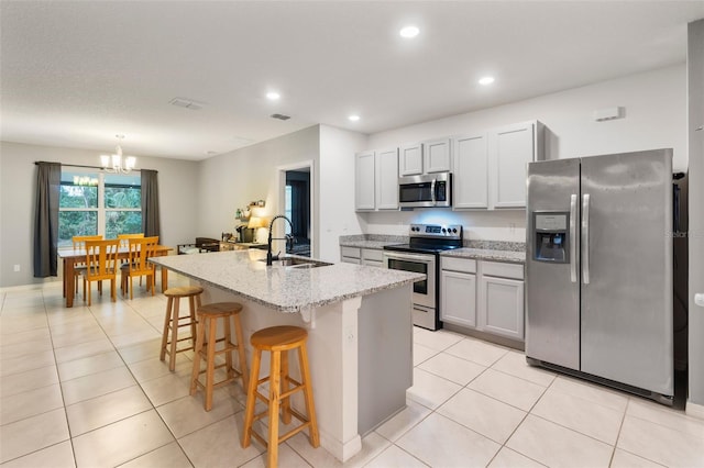 kitchen with a kitchen bar, stainless steel appliances, sink, light tile patterned floors, and a center island with sink