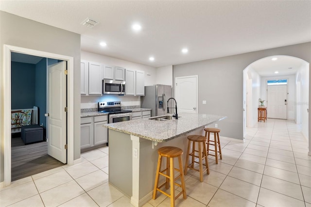 kitchen with an island with sink, light stone countertops, light tile patterned floors, a breakfast bar, and stainless steel appliances