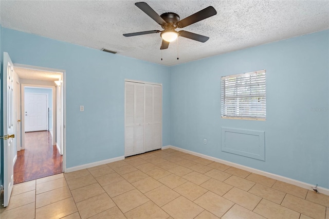 unfurnished bedroom with a textured ceiling, ceiling fan, light tile patterned flooring, and a closet