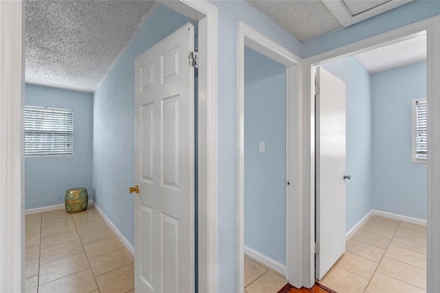 hallway with a textured ceiling and light tile patterned floors