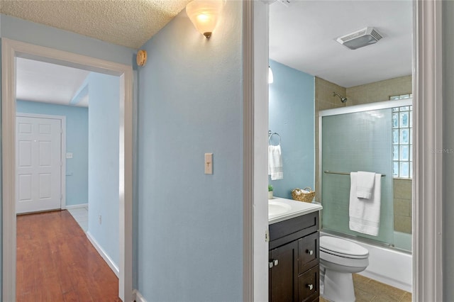 full bathroom featuring a textured ceiling, vanity, bath / shower combo with glass door, toilet, and hardwood / wood-style flooring