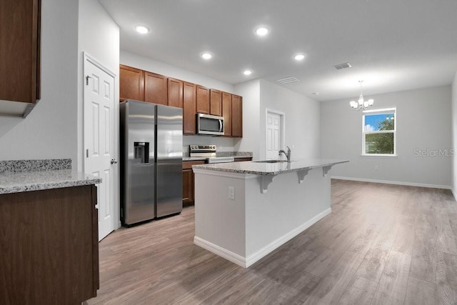 kitchen with light stone countertops, pendant lighting, wood-type flooring, stainless steel appliances, and a notable chandelier