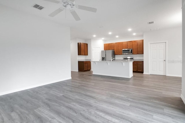 kitchen with appliances with stainless steel finishes, an island with sink, light wood-type flooring, ceiling fan, and a breakfast bar area