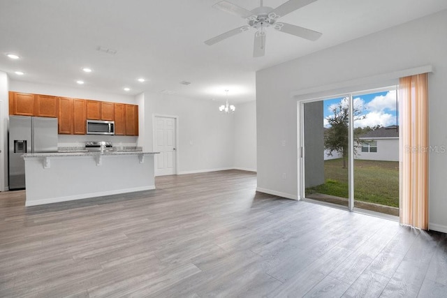 kitchen featuring a kitchen bar, light wood-type flooring, a kitchen island with sink, appliances with stainless steel finishes, and light stone counters