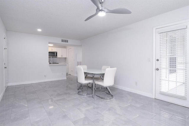 dining room with ceiling fan, sink, and a textured ceiling