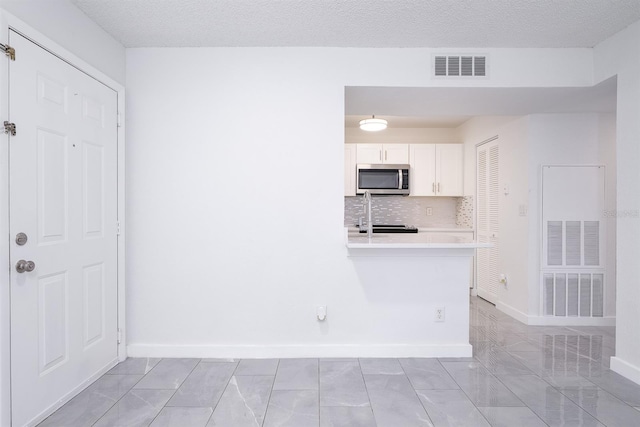 kitchen featuring a textured ceiling, white cabinets, backsplash, kitchen peninsula, and stove