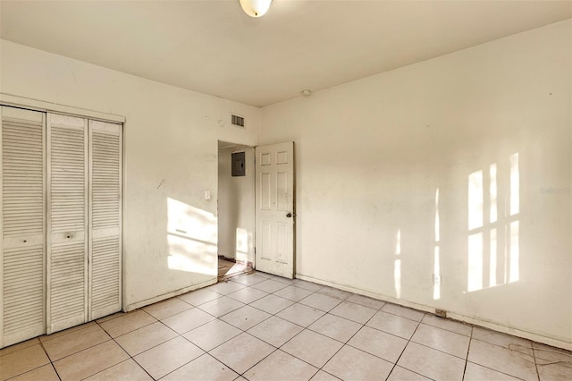 unfurnished bedroom with light tile patterned floors, a closet, and electric panel