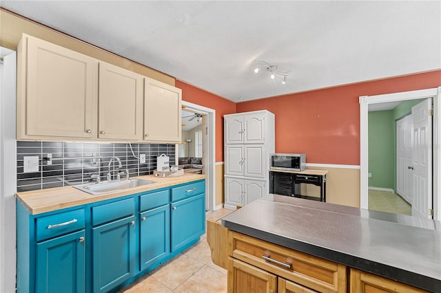 kitchen with blue cabinetry, light tile patterned floors, stainless steel microwave, decorative backsplash, and a sink