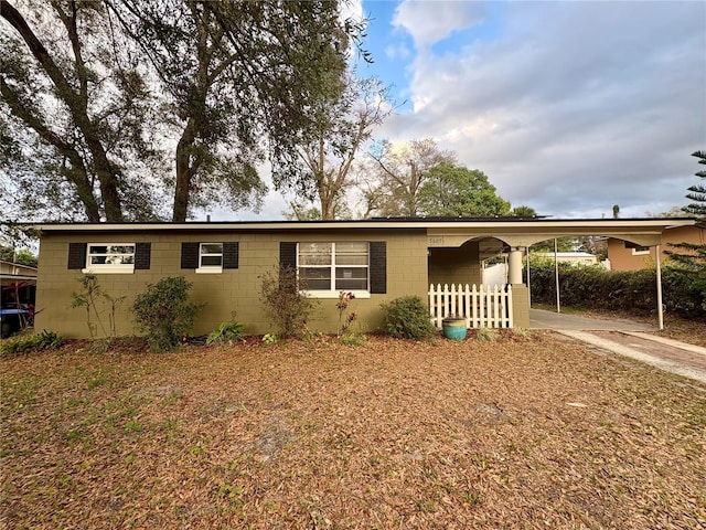 view of front of home with an attached carport, concrete block siding, fence, and concrete driveway