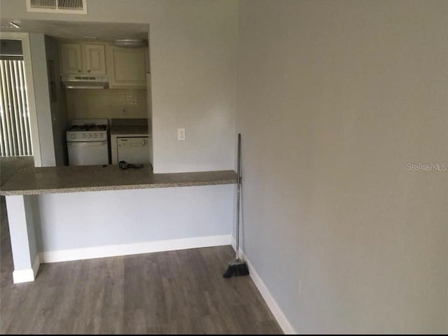 kitchen with dark wood-type flooring, cream cabinets, backsplash, and white gas stove