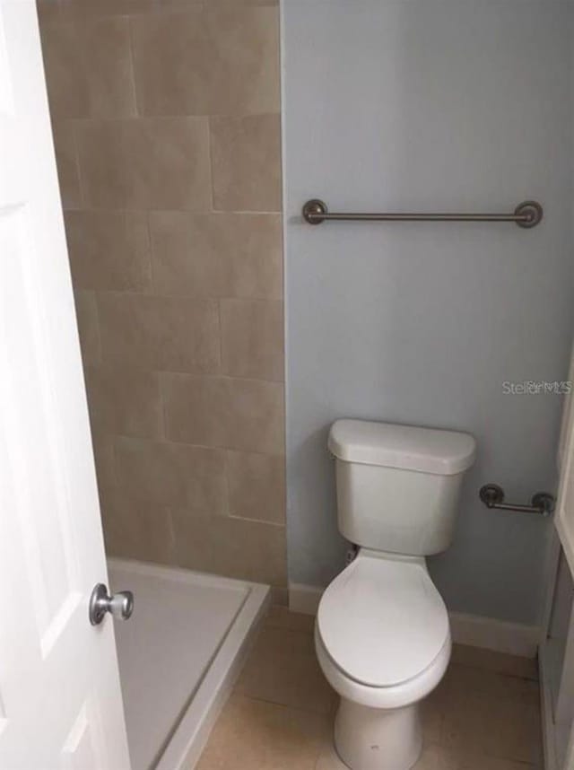 bathroom featuring toilet, tiled shower, and tile patterned floors